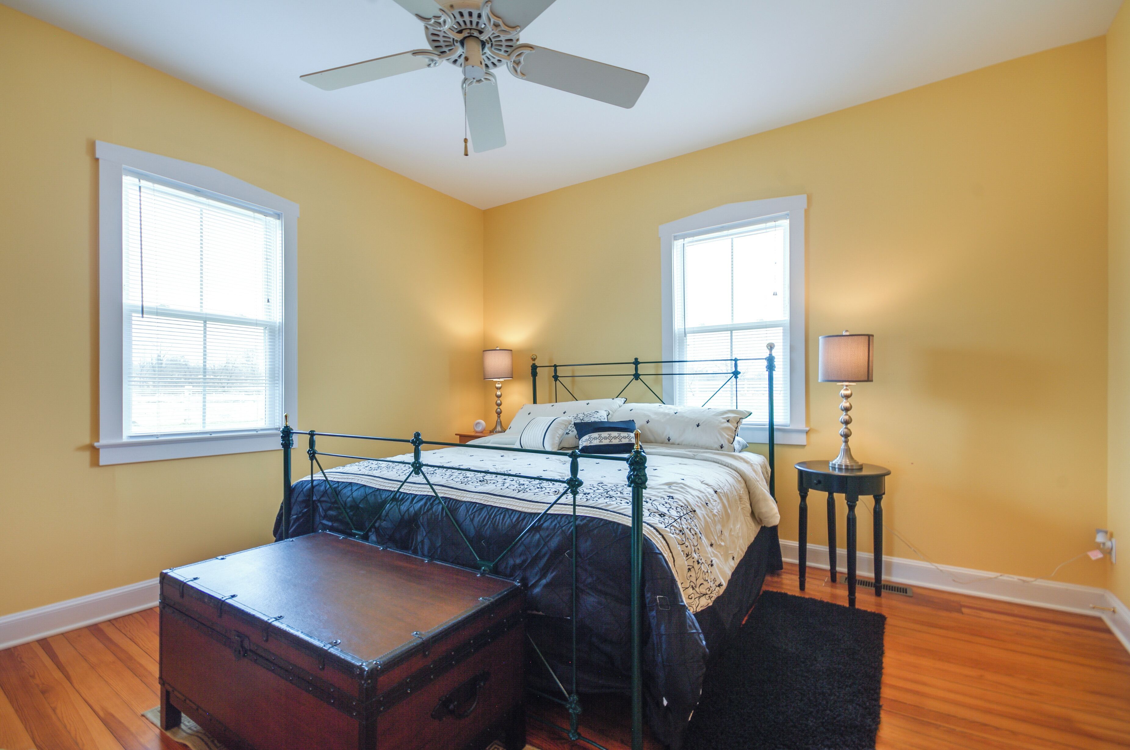 A bedroom with a bed, two bedside lamps, a wooden chest, and a ceiling fan.