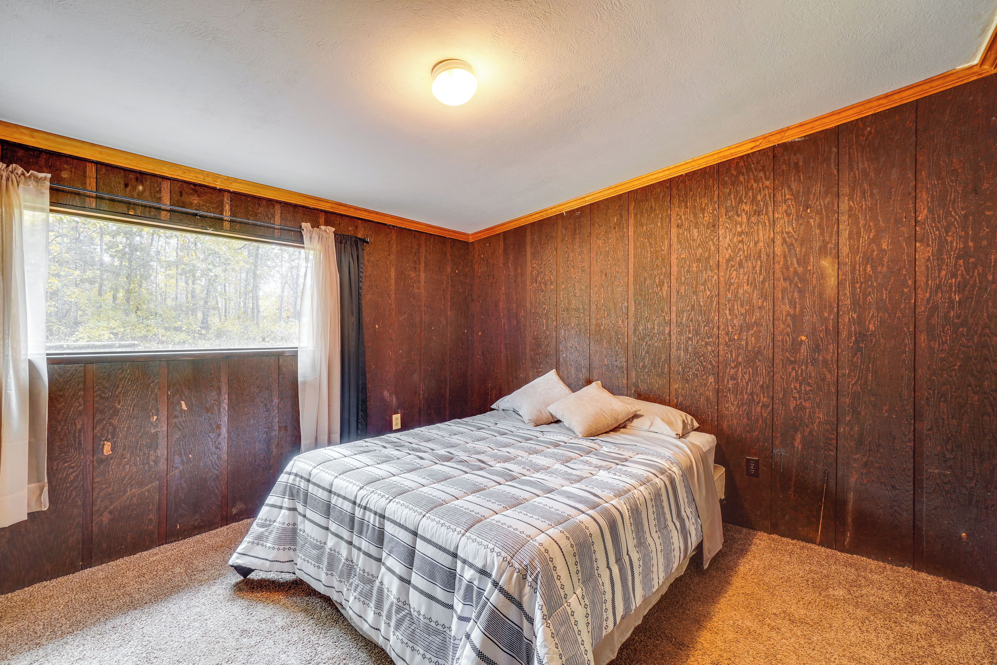 Une chambre avec un grand lit, des murs en bois, une fenêtre avec des rideaux et un luminaire au plafond.