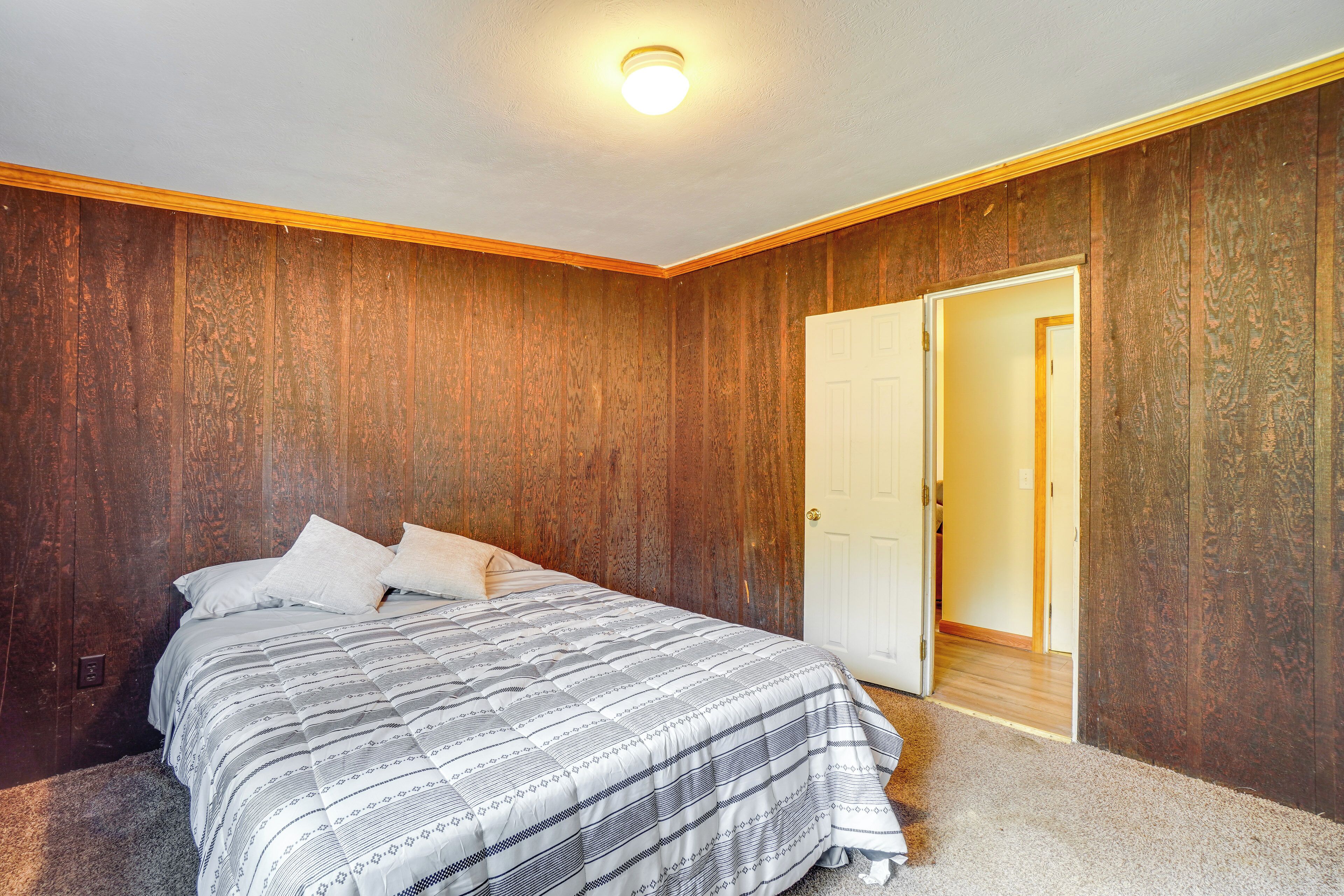 Un dormitorio con una pared de madera, una cama con colcha a rayas y una puerta blanca.