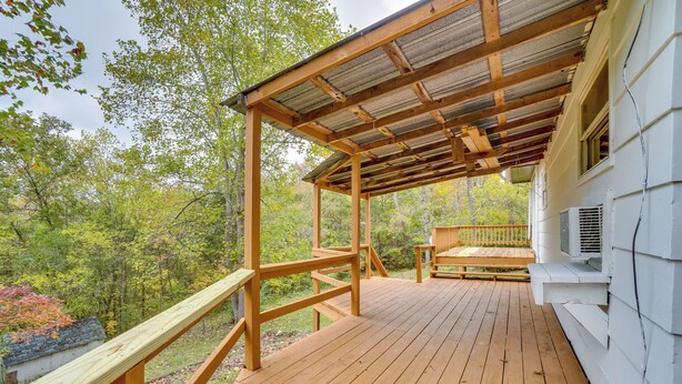 A wooden deck with a covered area and a bench, surrounded by trees. - Table Rock Lake Cabin w/ Deck & Bar! (Shell Knob)