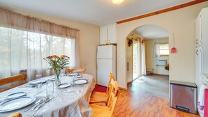 A dining area with a table set for four, wooden chairs, a white refrigerator, and a kitchen visible through an archway. - Table Rock Lake Cabin w/ Deck & Bar! (Shell Knob)