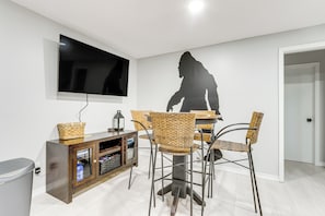 A dining area with a modern TV, wicker chairs, and a wooden cabinet.