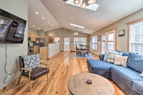 A spacious living area with a wooden floor, a blue sofa, a dining table, and a kitchen in the background.
