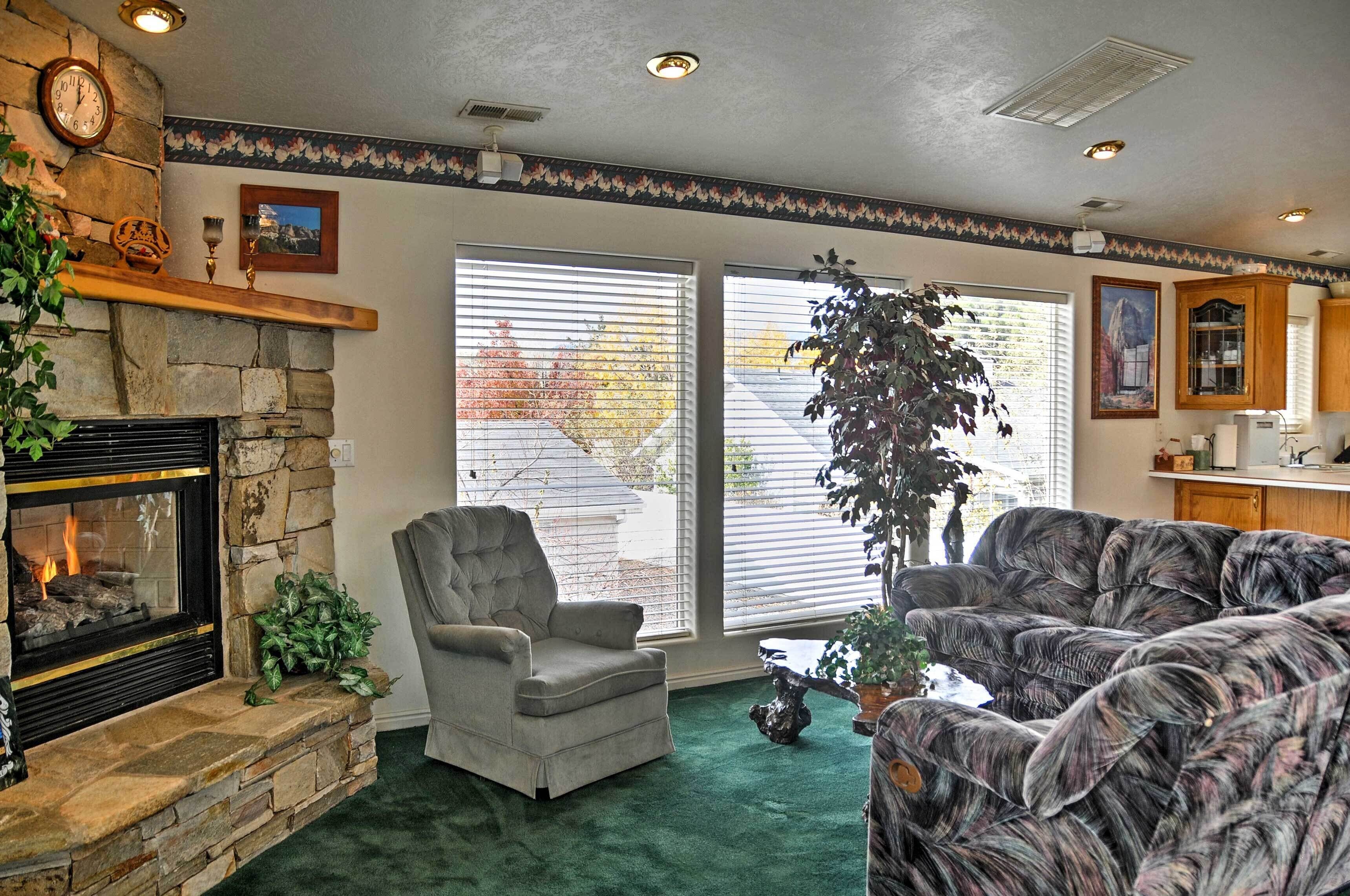A living room with a stone fireplace, a grey armchair, a patterned sofa, and a large potted plant.