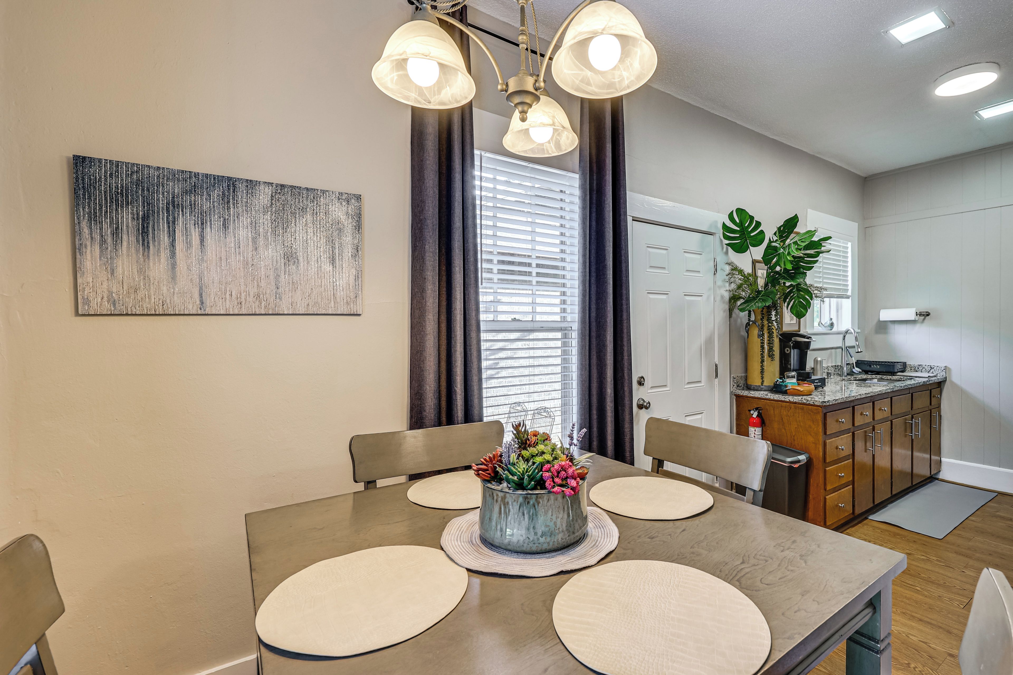 A dining area with a table, chairs, a vase with flowers, and a painting on the wall.