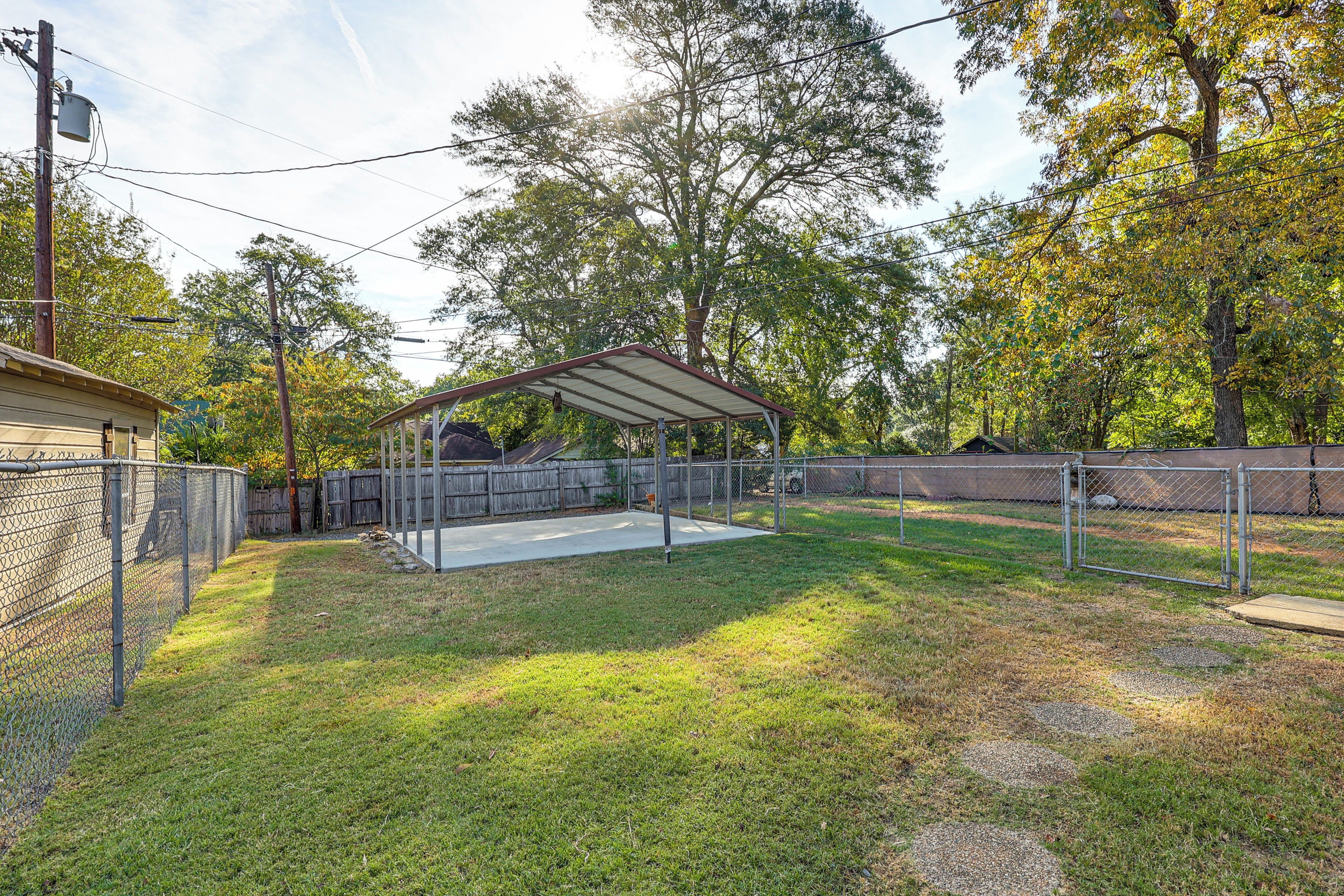 A fenced outdoor area with a covered seating area, a concrete path, and a building in the background.