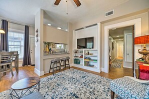 A modern living room with a flat-screen TV, a dining area with a wooden table and chairs, and a kitchen area with a countertop and bar stools. - Texarkana Pet-friendly Pad w/ Fenced Backyard (Texarkana)