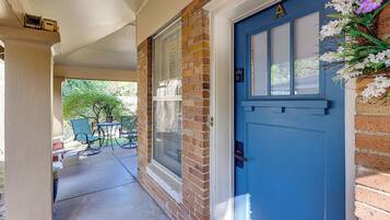 A blue door with a window, a brick wall, and a porch with chairs.
