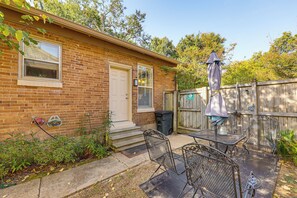 Une maison en briques avec une porte d’entrée, une fenêtre et un patio aménagé avec des chaises et une table en métal.