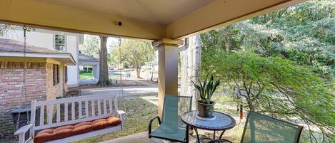 A covered porch with a swing, a table with chairs, and a potted plant.