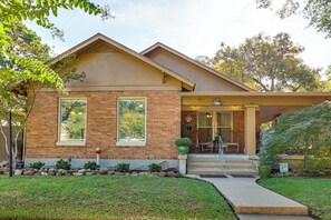 A two-story house with a brick facade, a front porch with chairs, and a well-maintained lawn.