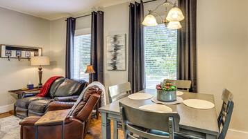 A modern living room with a leather sofa, a dining table with chairs, a lamp, and a painting on the wall.