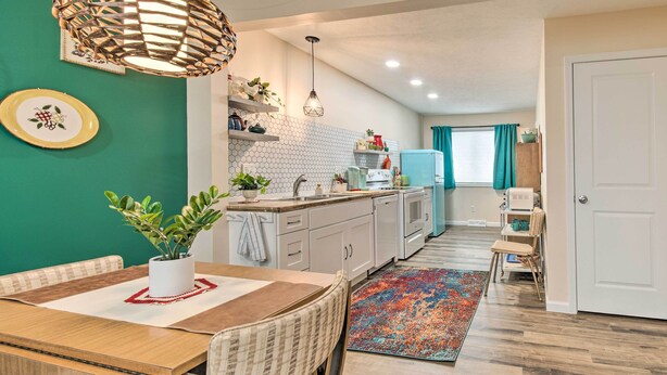 Une cuisine moderne avec des meubles blancs, une table à manger en bois et un tapis aux couleurs vives.