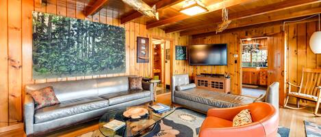 A cozy wooden cabin interior with a sofa, armchair, and a flat-screen TV.