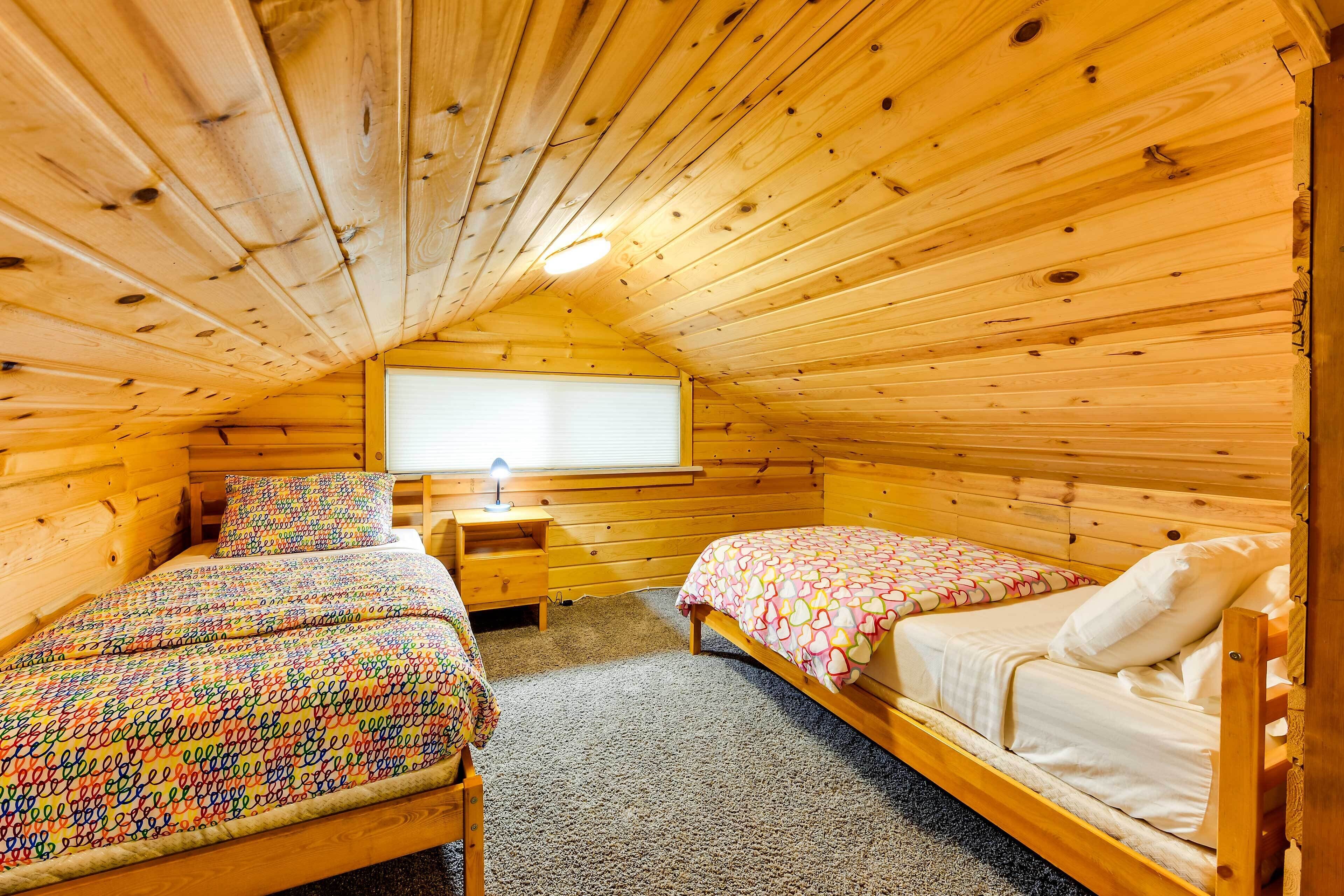 A cozy wooden cabin bedroom with two beds, a window, and a small bedside table.