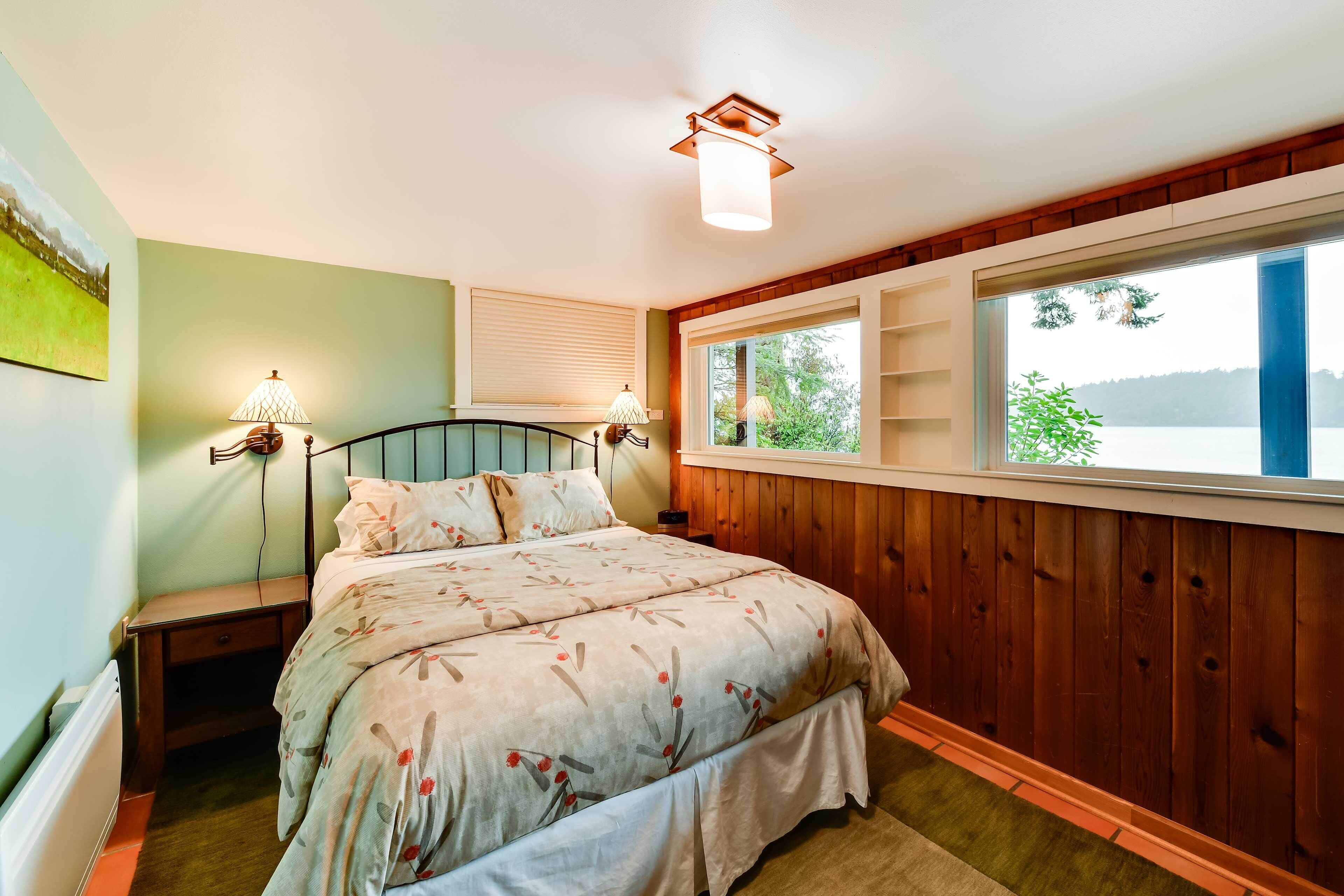 Ein Schlafzimmer mit Holz-Kopfteil, einem großen Fenster mit Blick auf Bäume und einem Bett mit floraler Bettwäsche.