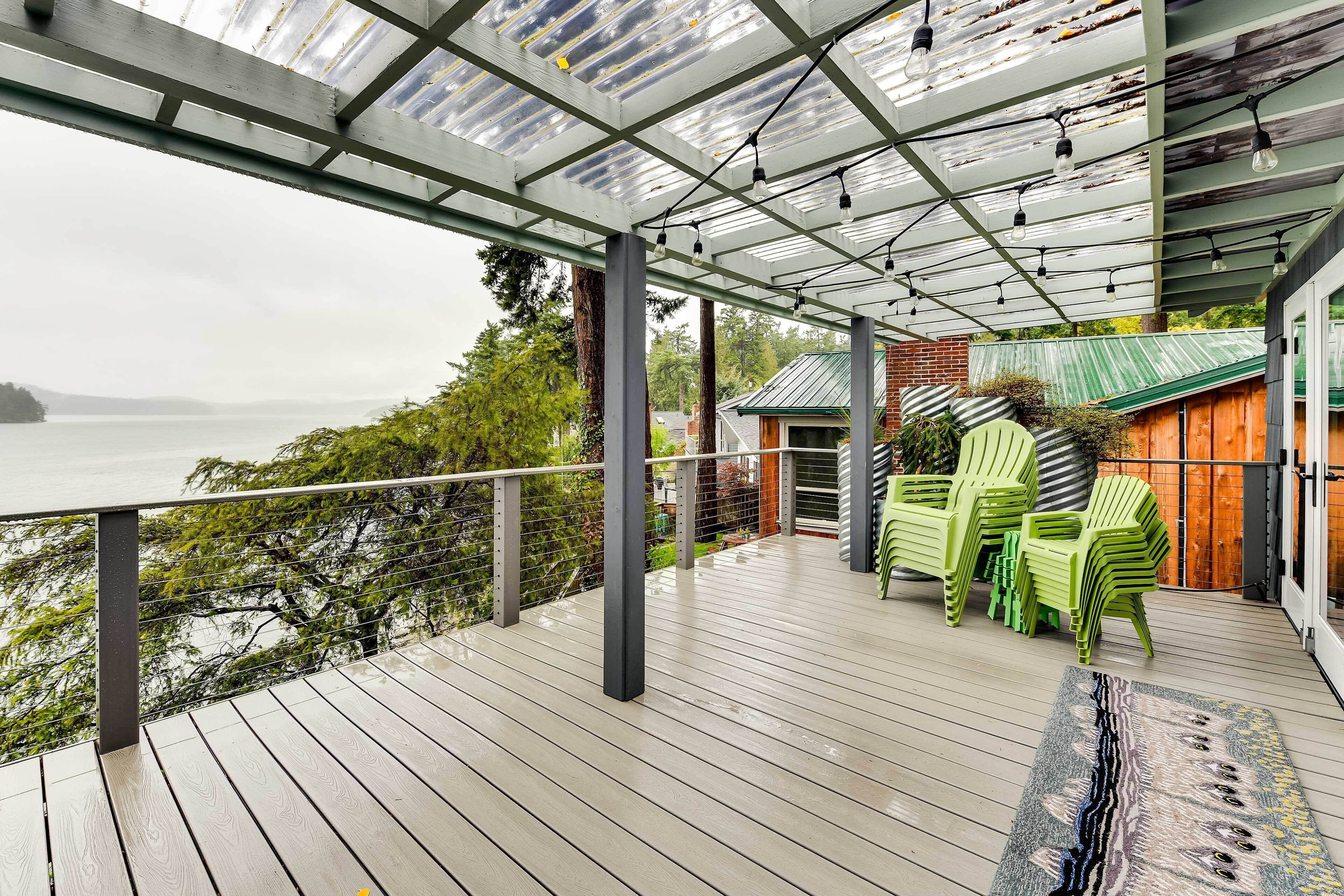 A covered deck with a view of the water, green chairs, and a patterned rug.