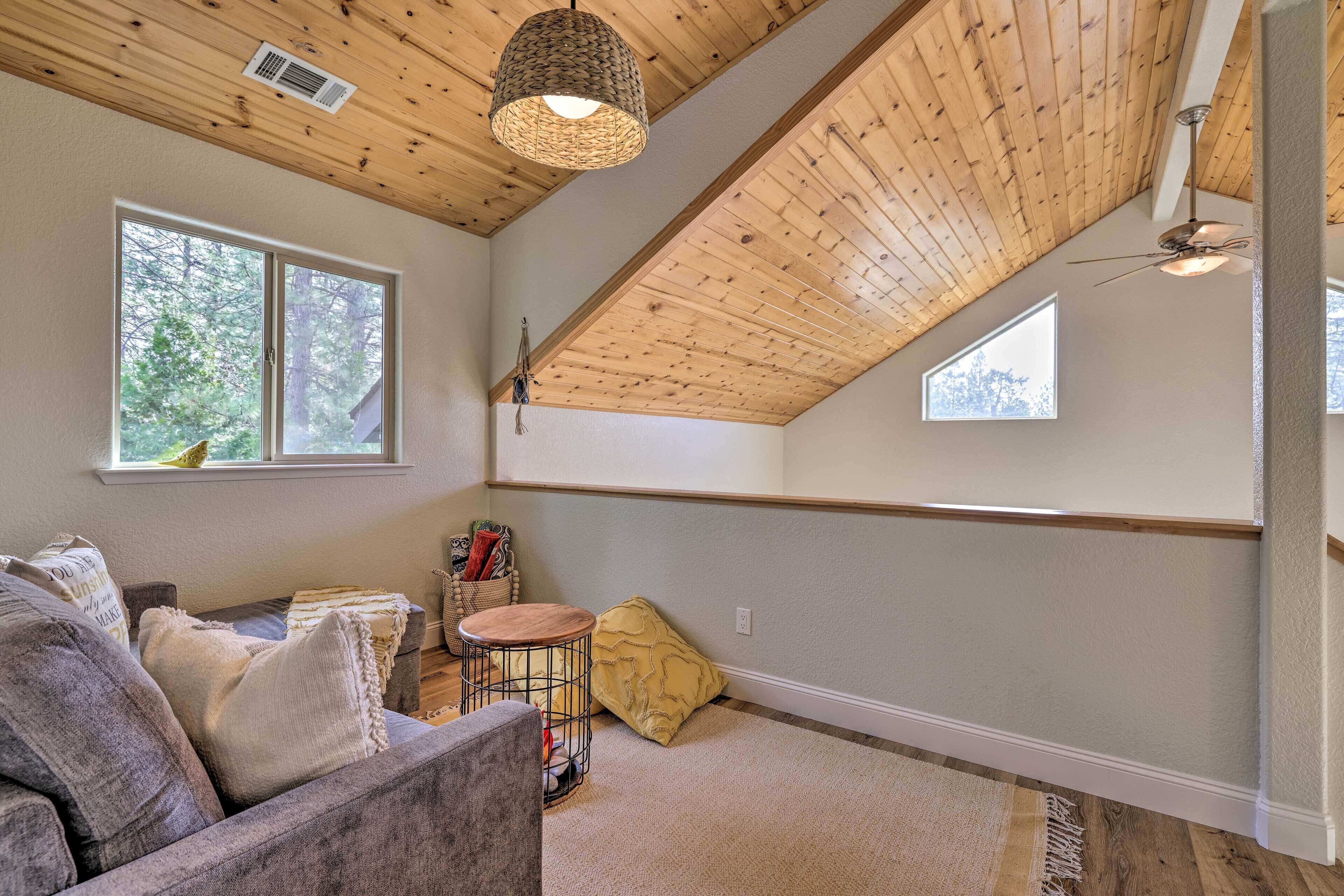 A cozy room with a sloped ceiling, a sofa, a small round table, and a window with a view of trees.