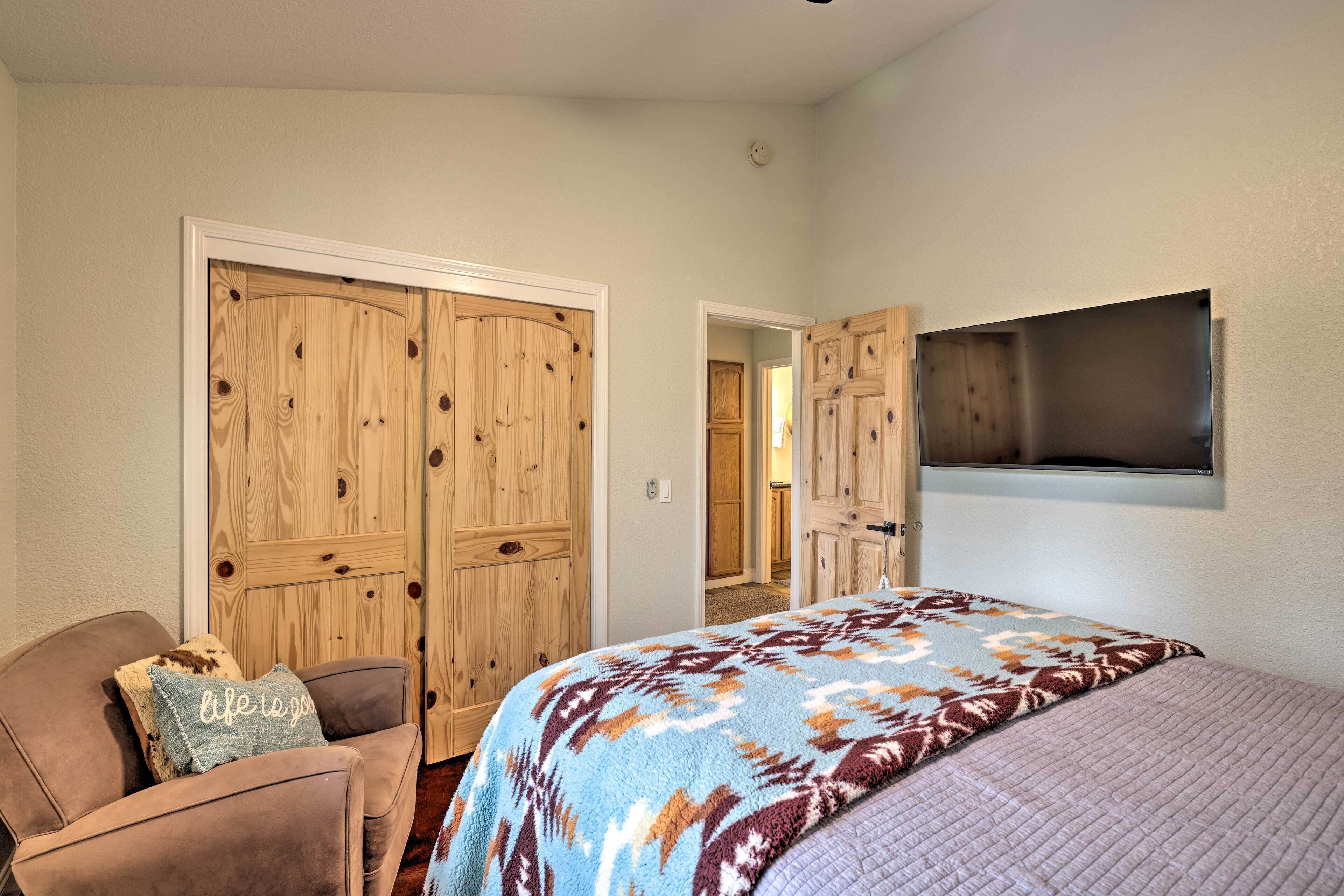 A bedroom with a bed, a chair, two wooden doors, and a mounted TV.