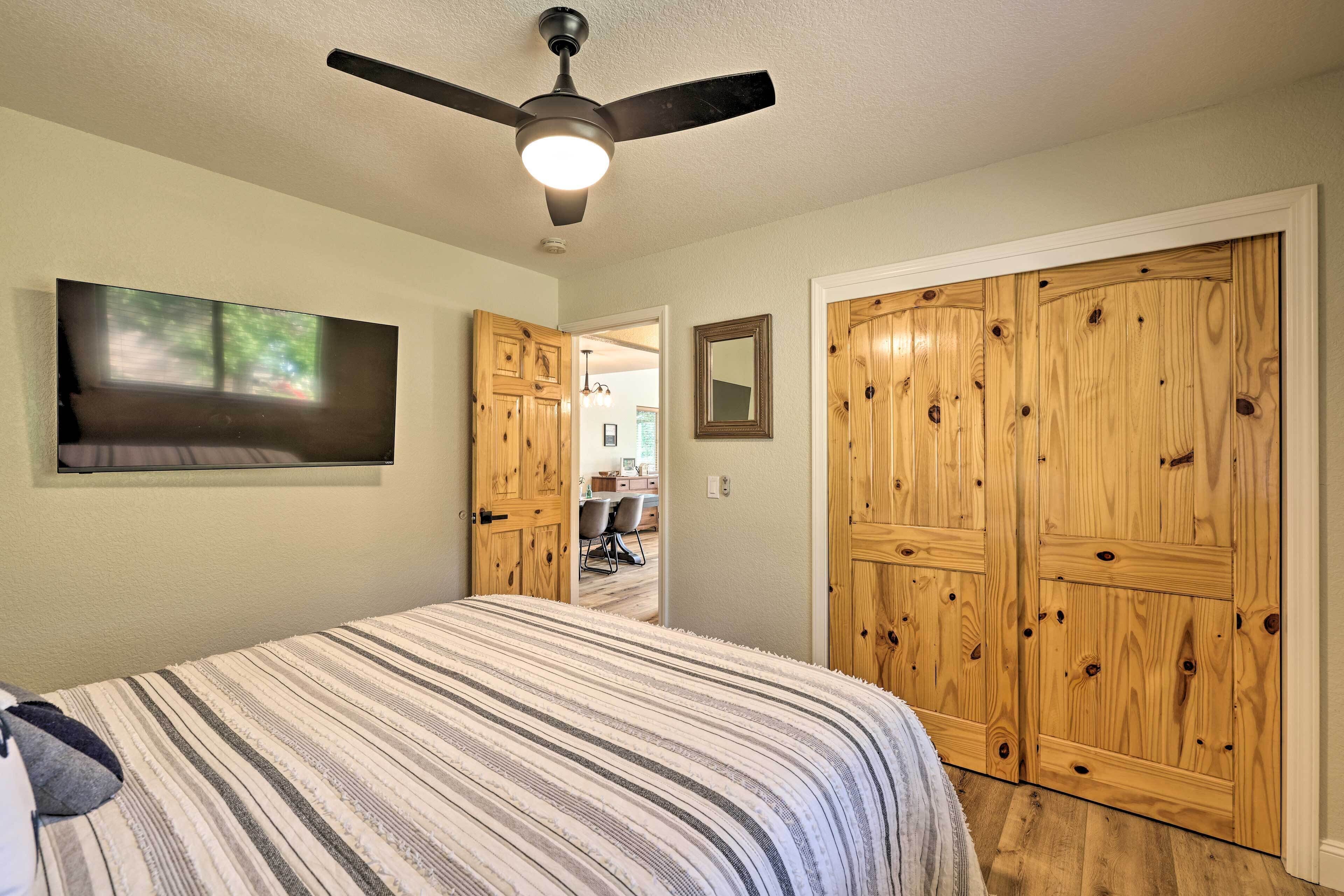 Ein Schlafzimmer mit Bett, Holzschrank, Deckenventilator und einem an der Wand befestigten Fernseher.
