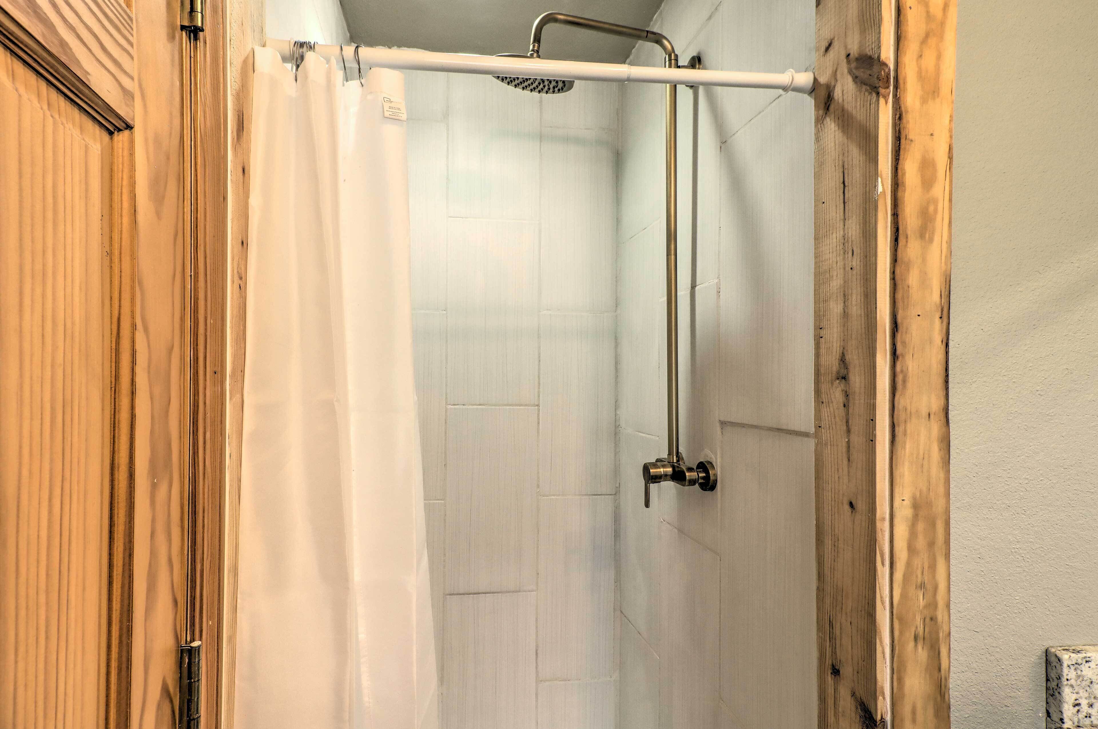 A shower area with a wooden door, a white shower curtain, and a metal shower head.