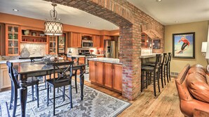 A spacious kitchen with a brick archway, wooden cabinets, a central island, and a dining area with a leather couch. - Modern Home w/ Patio: 3 Mi to Beaver Creek Resort! (Avon)