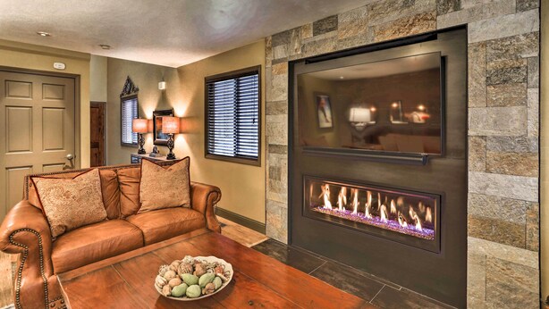 A living room with a leather sofa, a wooden coffee table, a fireplace, and a stone accent wall. - Modern Home w/ Patio: 3 Mi to Beaver Creek Resort! (Avon)