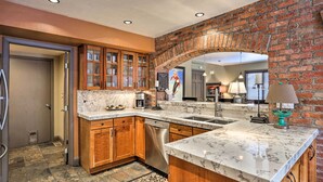 A kitchen with wooden cabinets, a marble countertop, a brick wall, and a built-in dishwasher. - Modern Home w/ Patio: 3 Mi to Beaver Creek Resort! (Avon)
