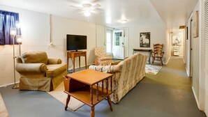 A living room with a sofa, armchair, and a small wooden table. There is a ceiling fan, a television, and a door leading to another room. - Lexington Apt Rental Near VA Military Institute! (Lexington)