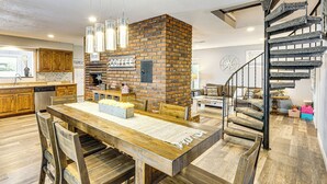 A spacious kitchen with a brick wall, wooden dining table, and a spiral staircase. - Beach + Dock! Lakefront Ozarks A-frame Retreat (Linn Creek)