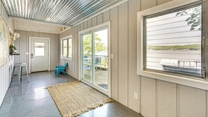 A hallway with a concrete floor, a woven rug, a door, and a window with a view of a dock and greenery. - Beach + Dock! Lakefront Ozarks A-frame Retreat (Linn Creek)