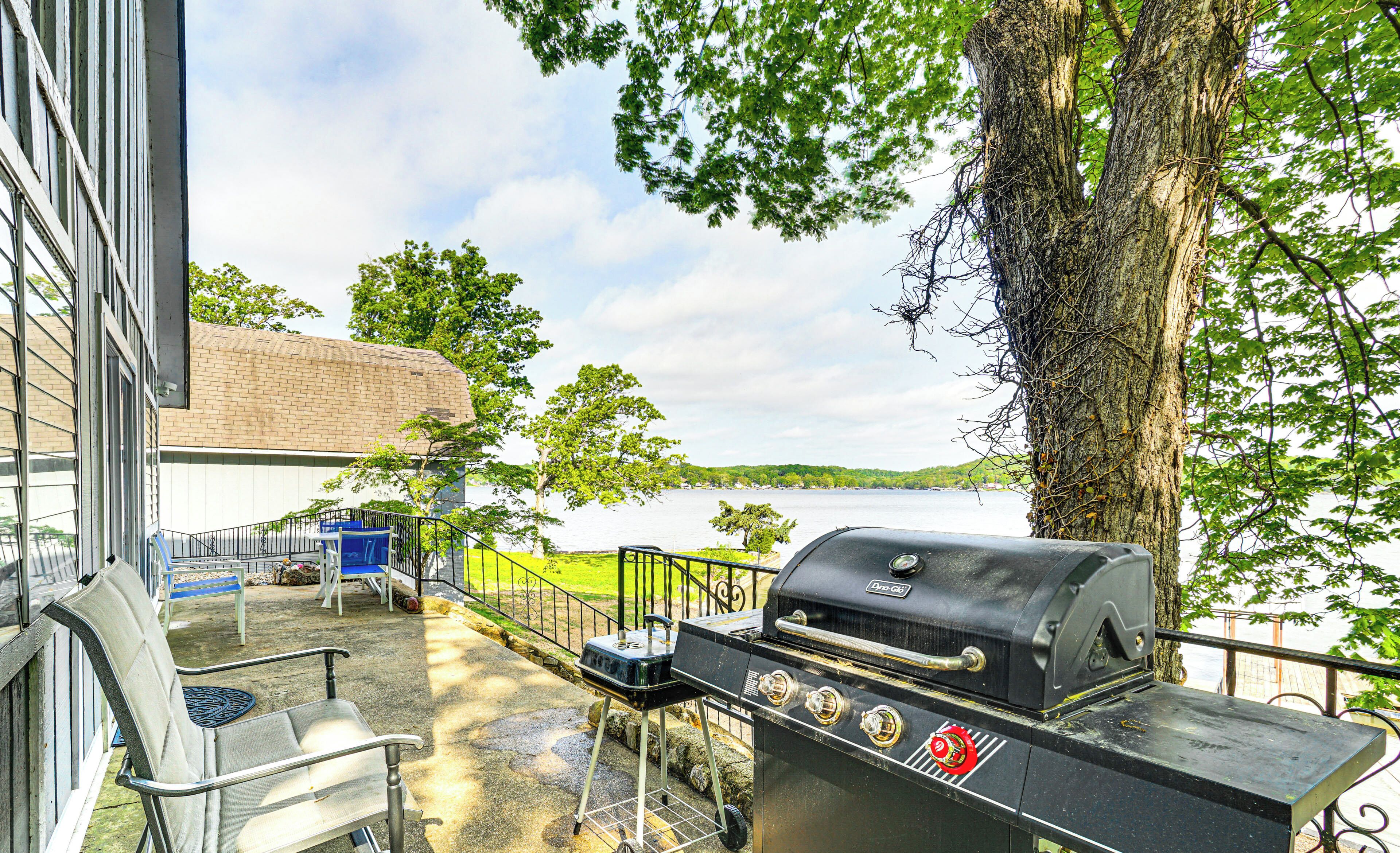 A patio with a grill, a chair, and a view of a lake.