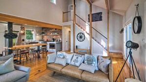 Ein geräumiger Wohnbereich mit Holzboden, einer Couch mit Zierkissen, einer Küche im Hintergrund und einer Treppe mit einem verzierten Funktionsrad.