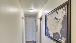 Un pasillo con un mapa enmarcado en la pared, una puerta blanca al final, y una lámpara en el techo.