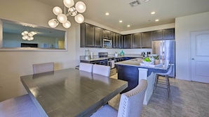 Une cuisine moderne avec des meubles de couleur sombre, un îlot central et un coin repas comprenant une grande table et des chaises.