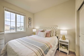 A bedroom with a large bed, a nightstand with a lamp, a window with blinds, and a view of the outside. - Visalia Home w/ Yard: 4 Mi to Downtown! (Visalia)