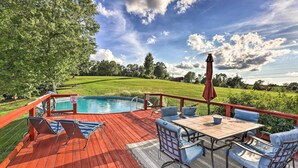 Eine Holzterrasse mit Pool, Gartenmöbeln und Blick auf ein Wiesenfeld.