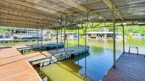 Une zone de quai abritée, dotée d’une terrasse en bois, de garde-corps en métal et offrant une vue sur une maison située de l’autre côté de l’eau.