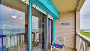 Ein Balkon mit Blick auf den Strand, ein Schild mit der Aufschrift 'The Beach' sowie zwei Stühle mit blauen Kissen.