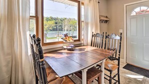 A dining area with a wooden table and chairs, a window with curtains, and a view of a lake. - Rockaway Beach House w/ Fire Pit & River View! (Rockaway Beach)