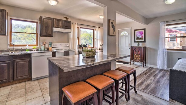 A spacious kitchen with dark wooden cabinets, a large island with stools, and a view of the outdoors through the windows. - Rockaway Beach House w/ Fire Pit & River View! (Rockaway Beach)