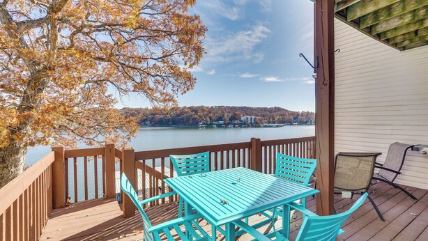 Une terrasse en bois avec une table et des chaises turquoise, donnant sur un lac aux couleurs automnales.