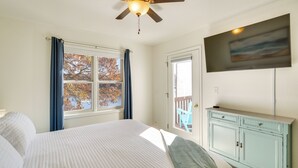Une chambre à coucher avec un lit, un ventilateur de plafond, une fenêtre avec des rideaux, une porte, un téléviseur et une commode bleu clair.