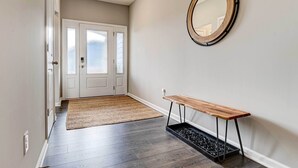 A hallway with a wooden bench, a round mirror, and a doormat leading to a door with frosted glass panels. - Spacious Home w/ Patio Near Fishers! (Fortville)