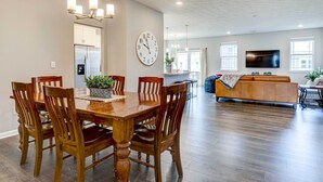 A spacious living area with a wooden dining table, chairs, a sofa, and a TV mounted on the wall. - Spacious Home w/ Patio Near Fishers! (Fortville)