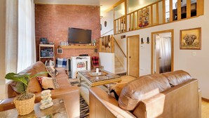 A spacious living area with a leather sofa, a coffee table, and a brick wall. - Wisconsin Cabin w/ ATV Trails, Near Lake Arbutus! (Merrillan)