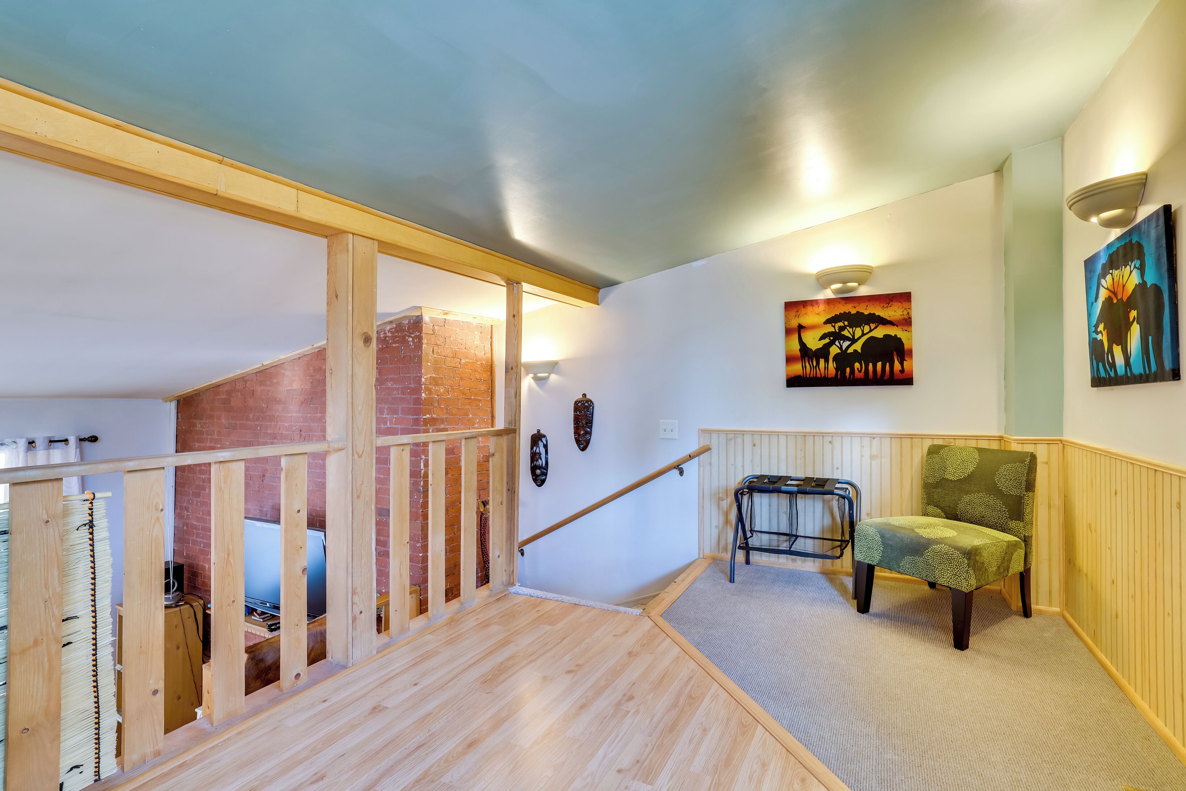 A staircase with wooden railings, a chair, and artwork on the walls.