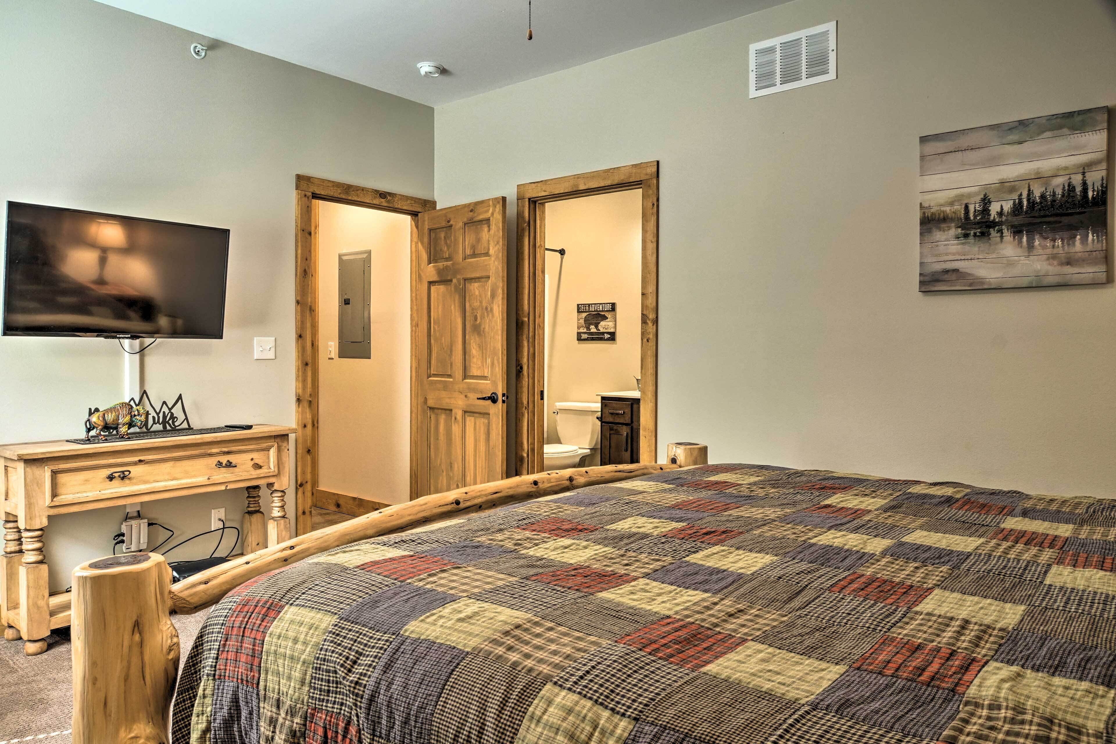 A bedroom with a large bed, a wooden dresser, a television, and a door leading to a bathroom.