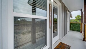 A covered porch with a welcome sign, large windows, and a view of the backyard.