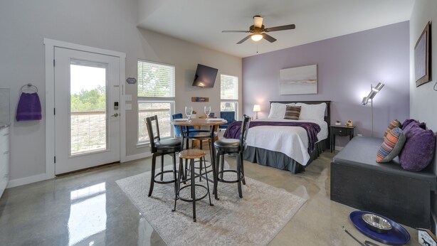 A bedroom with a bed, a desk, chairs, a ceiling fan, and a window.